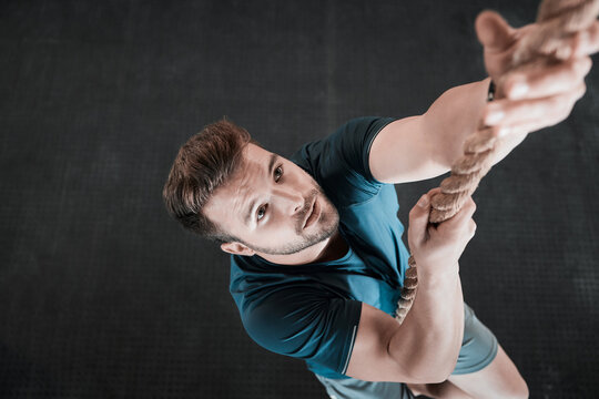 Studio, fitness and man on rope for climbing challenge, health and wellness for muscle workout from above. Gym, exercise and strong climber with body training, performance or power on gray background