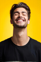 Obraz premium Radiant Joy: A Young Man's Infectious Smile. Carefree young man smiling with his eyes closed in a studio. Happy young man standing alone against a yellow background. generative AI