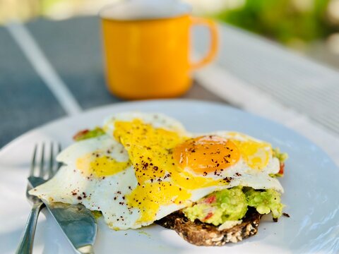 Close-up of an avocado, tomato and spring onion toast with a fried egg, sumac and a cup of tea on a garden table in summer