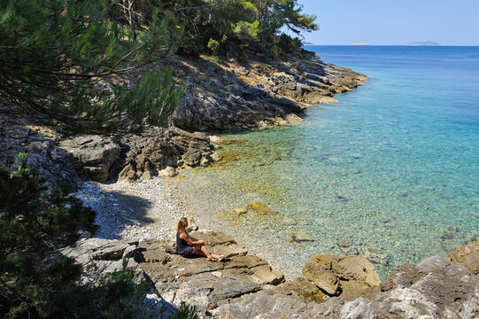 Woman sitting on rocks at a creek of Mrcara islet at the north-west of Lastovo island, Croatia, Southeast Europe