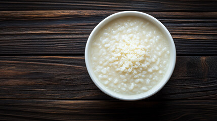 Creamy rice porridge with freshly grated cheese in a white bowl on a dark wooden table