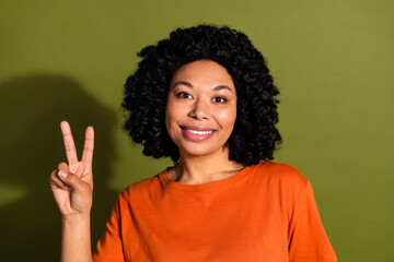 Photo portrait of pretty young girl show v-sign wear trendy orange outfit isolated on khaki color background