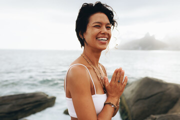 Smiling woman enjoying seaside yoga pose at the beach on a sunny vacation day