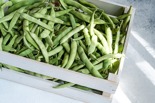 Overhead view of fresh organic runner beans in a wooden crate on a table