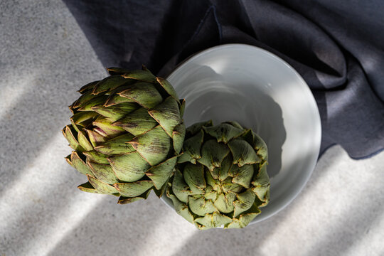 Close-up overhead view of two artichokes in a bowl in sunlight