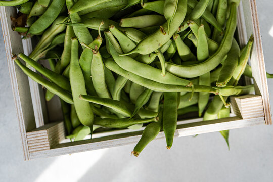 Overhead view of fresh organic runner beans in a wooden crate on a table