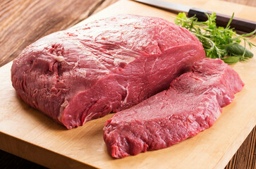 Raw sirloin beef steak and the round of a cow offered as close-up on a wooden cutting board