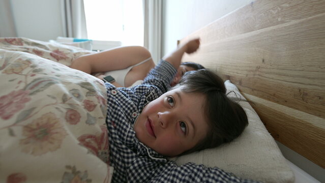 Young boy stretching arms in bed, ready to get up, with sleeping mother and baby, early morning family scene, cozy and loving environment, tender family moments, nurturing care, motherly affection
