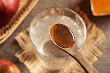 A spoonful of apple cider vinegar above a glass of water