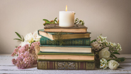 Stack of Vintage Books Surrounded by Flowers with a White Candle on Top