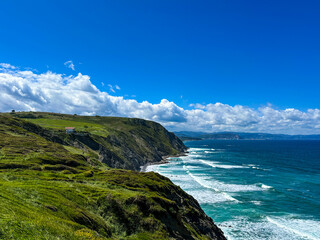 The green and steep coastline of the Atlantic Ocean. A lonely little house stands near the cliff.