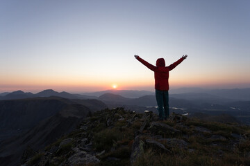 A person in a red jacket is standing on a mountain top