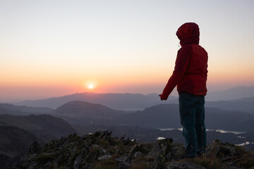 Naklejka premium A person is standing on a mountain top, looking out at the sunset
