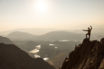 A man is standing on a mountain top, with a clear blue sky in the background