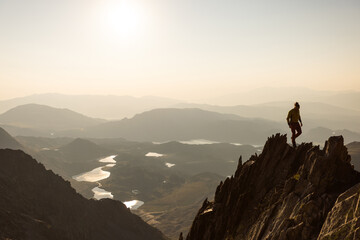 A man is standing on a mountain top, looking out over a beautiful landscape