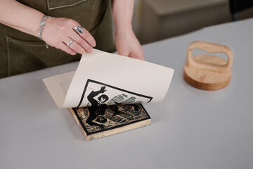 High angle of hands of young creative woman taking paper off wooden workpiece with cut handmade artwork after printing