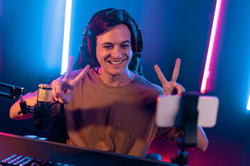 Host channel of gaming smart streamer playing online game, wearing headphone with viewers live steaming on media social online by smartphone talking with team player at neon lighting room. Pecuniary.