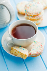 Tea cup and sweet dessert with sugar coating on blue table.
