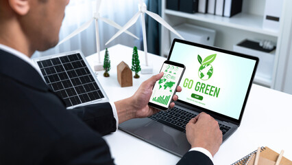 Businessman working in office developing plan or project on eco-friendly alternative energy with solar cell technology display on computer screen for greener environment as apart of CSR effort. Gyre