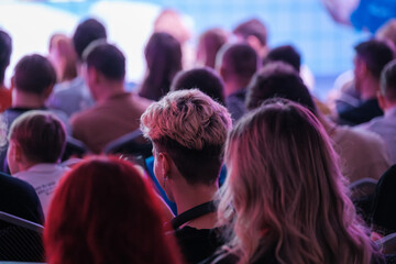 Large group of people attending conference focusing on stage, highlighting educational and...