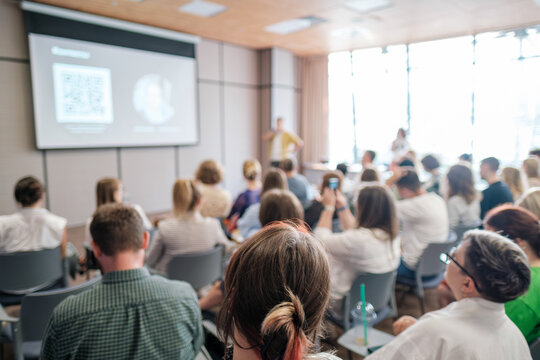 Conference attendees focusing on speaker during presentation with projected slides. Engaging business meeting atmosphere with active participation.