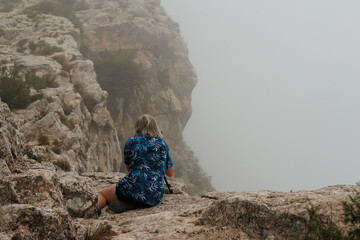 Fotógrafa sentada en la roca fotografiando el paisaje con nubes y niebla en el parque natural...