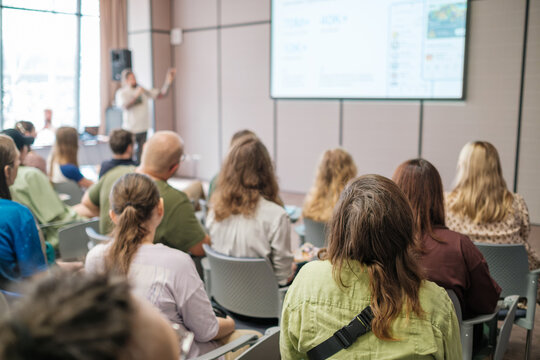 Conference room filled with attentive participants listening to presenter delivering engaging lecture on various topics. Learning atmosphere captured in modern professional environment.