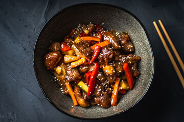 A traditional Chinese dish of pork in a sweet and sour sauce Kubero in a bowl with Chinese chopsticks on a dark gray background. Copyspace.