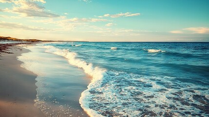  A stunning beach scene with crashing waves approaching the shoreline and a distant lighthouse illuminated on a bright sunny day