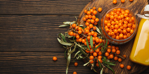 Sea buckthorn healthy drink in bottle, ripe berries in glass jar and branches with leaves top view...