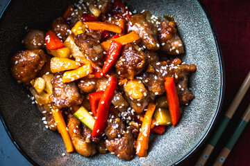 Pork in sweet and sour sauce with pineapple, capsicum, ginger in a bowl on a gray background. Copyspace. Close-up.