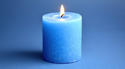   A blue candle with one lit candle is on a blue surface amidst a blue backdrop
