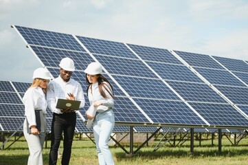 Group of multi ethnic people and safety helmets staring at solar farm.