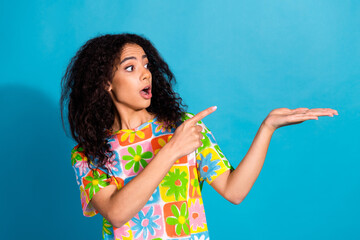 Photo of cheerful impressed lady dressed flower print t-shirt pointing finger holding arm empty space isolated blue color background