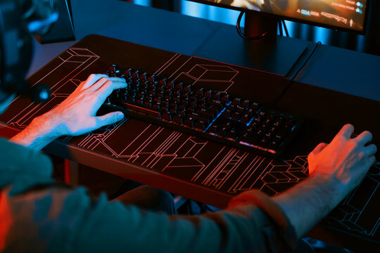 Cropped host channel of young gaming streamer playing fighting Moba at battle arena game with multiplays team on blurred pc screen with back side image at neon digital light modern room. Gusher.