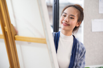 Young serious Asian woman Artist painting artwork at home workspace.