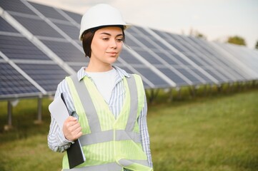 Portrait of beautiful female engineer technologist standing among solar panels