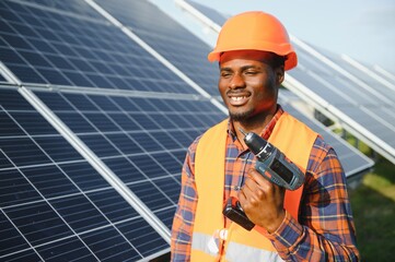 African american man in safety helmet on solar panels with screwdriver. Competent technician using...