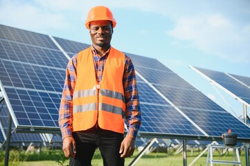 African american man in safety helmet on solar panels with screwdriver. Competent technician using tools while performing service work on station