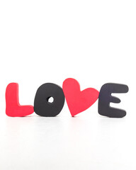 Word LOVE made of red and black volumetric letters and heart on white background. Valentine's day, love day and wedding concept. Vertical photo. High quality photo