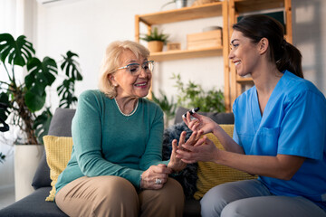 A cheerful caucasian nurse in scrubs provides home health care by checking the blood sugar level of...