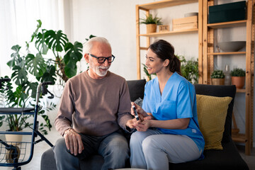 Fototapeta premium A cheerful caucasian nurse in blue scrubs provides professional in-home care for a senior male patient by checking his blood sugar levels in a comfortable apartment setting.