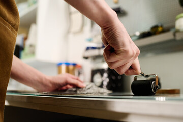 Hand of young unrecognizable craftswoman or female worker of printing house applying black ink on transparent glass with paintroller
