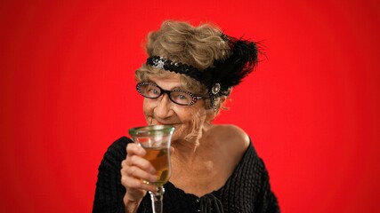 Smiling portrait of fun elderly old woman drinking wine and smiling wearing wig and glasses isolated on red background.