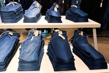 An assortment of jeans is carefully stacked on a shelf in a clothing store.