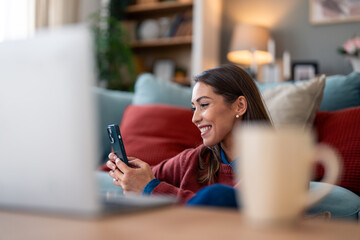 An enthusiastic Caucasian female multitasks, navigating both her smartphone and laptop while...