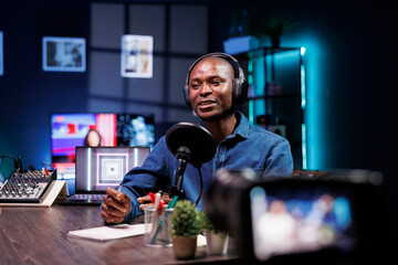 African American man uses a professional camera to record a vibrant vlog session at home. He engages with his digital audience through a live stream on his online channel.