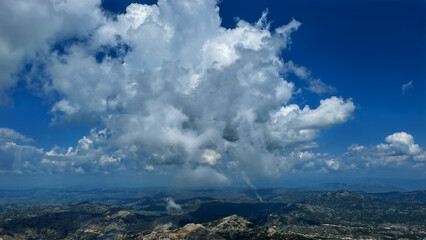 Breathtaking view of a massive cloud formation towering over a rugged mountain landscape under a deep blue sky. The grandeur of nature and the vastness of the open sky.