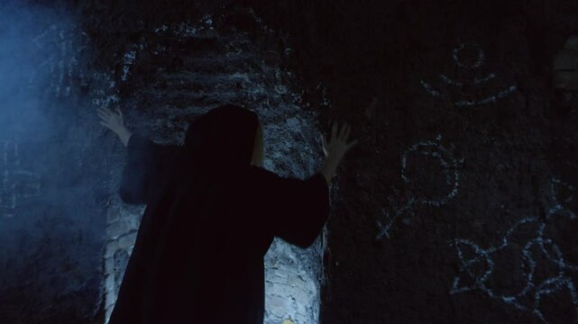 Woman in black robes touching cave walls