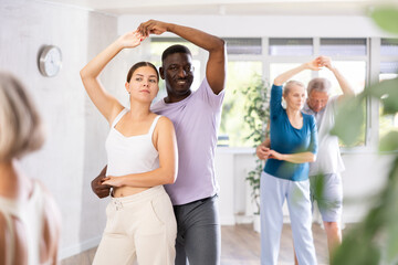 Dynamic young and mature attendees of dancing courses training poses of Waltz in dance hall